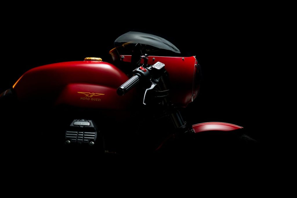 Elegant Moto Guzzi motorcycle in dramatic low light with red highlights.