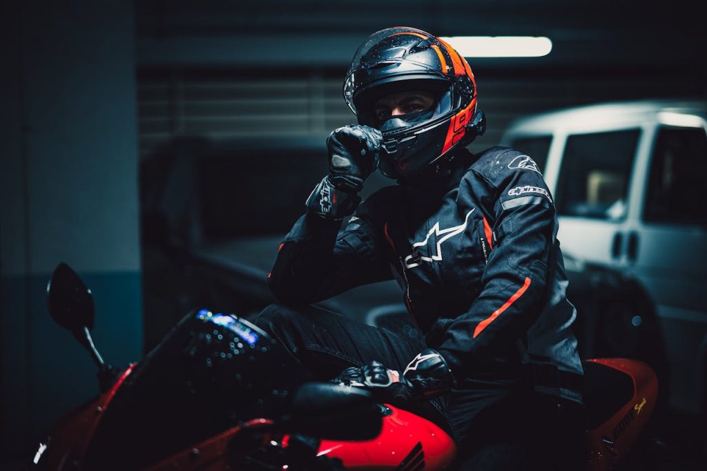 Motorcyclist in protective gear poses on red bike in dimly lit urban garage.