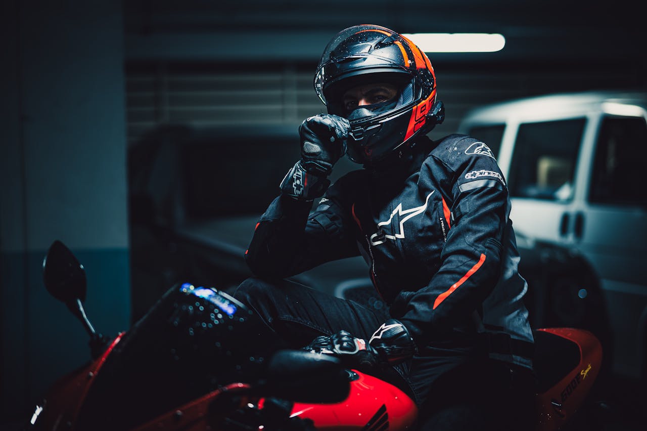 Motorcyclist in protective gear poses on red bike in dimly lit urban garage.